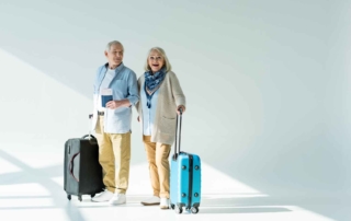 Man and woman elderly couple standing in front of white wall with black and teal suitcases