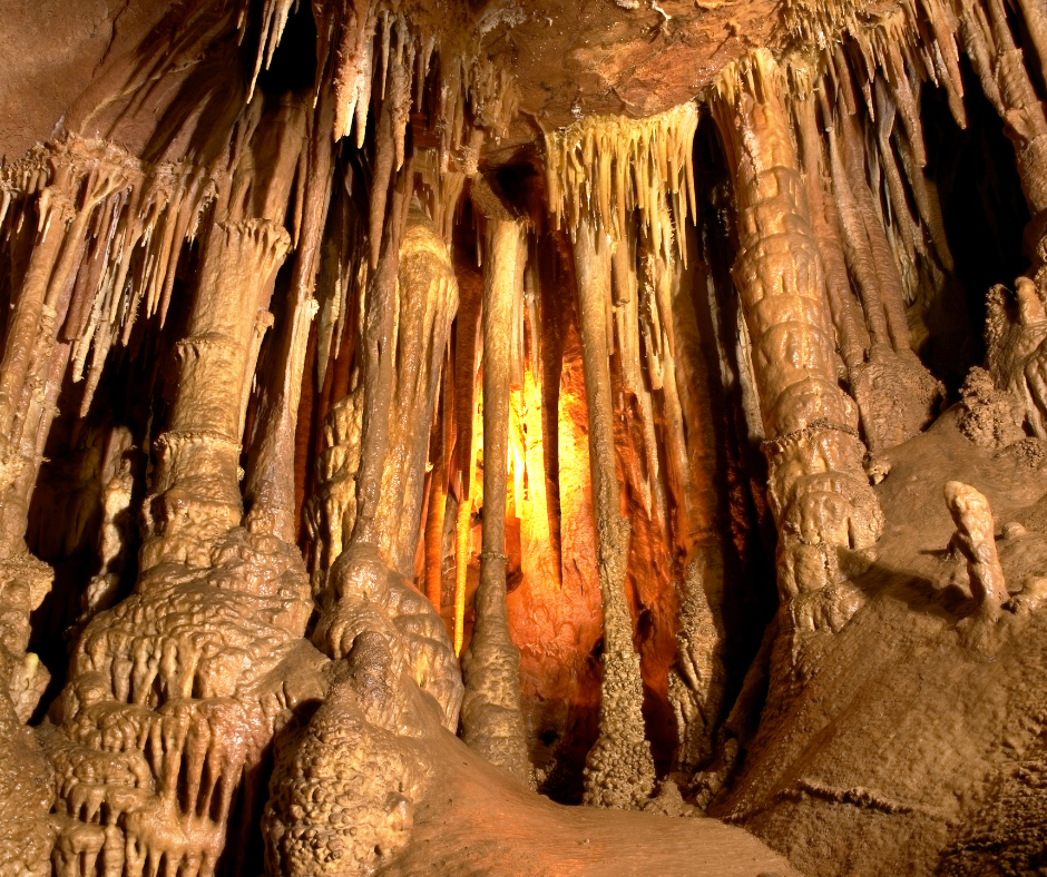 A stalactite cave with various sizes of stalactites and stalagmites illuminated by warm, orange light.