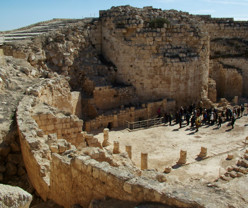 A group of people exploring the ruins of Herodium architecture in the West Bank with tall walls and broken columns.
